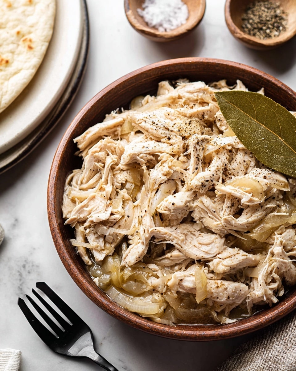 A large brown bowl filled with shredded light beige chicken mixed with finely chopped translucent onions, sprinkled with black pepper, and topped with a green bay leaf on the left side; a black spoon rests inside the bowl on the right; above to the left, a white plate with more shredded chicken and a black fork placed on it; to the upper right, a small white bowl with coarse salt and black pepper; all set on a white marbled surface next to a white cloth with black stripes; photo taken with an iphone --ar 4:5 --v 7