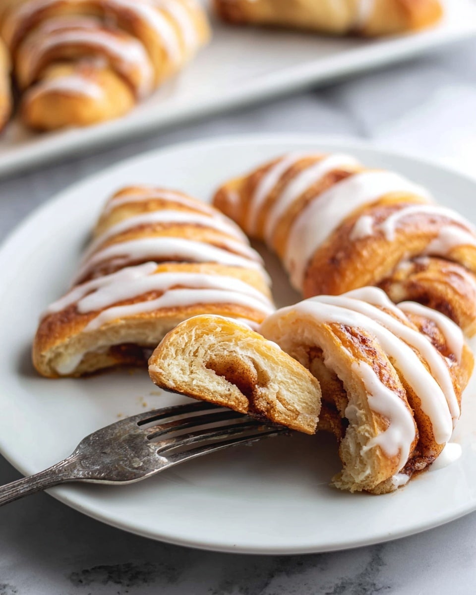 The image shows a close-up of several golden brown crescent rolls arranged on a black baking tray lined with a mesh baking mat. Each crescent roll is covered with thick white icing drizzled unevenly, creating soft, glossy lines and small pools of icing around the rolls. The rolls have a slightly crisp texture with some visible darker brown spots on the crust. The background surface is a white marbled texture. Photo taken with an iphone --ar 4:5 --v 7