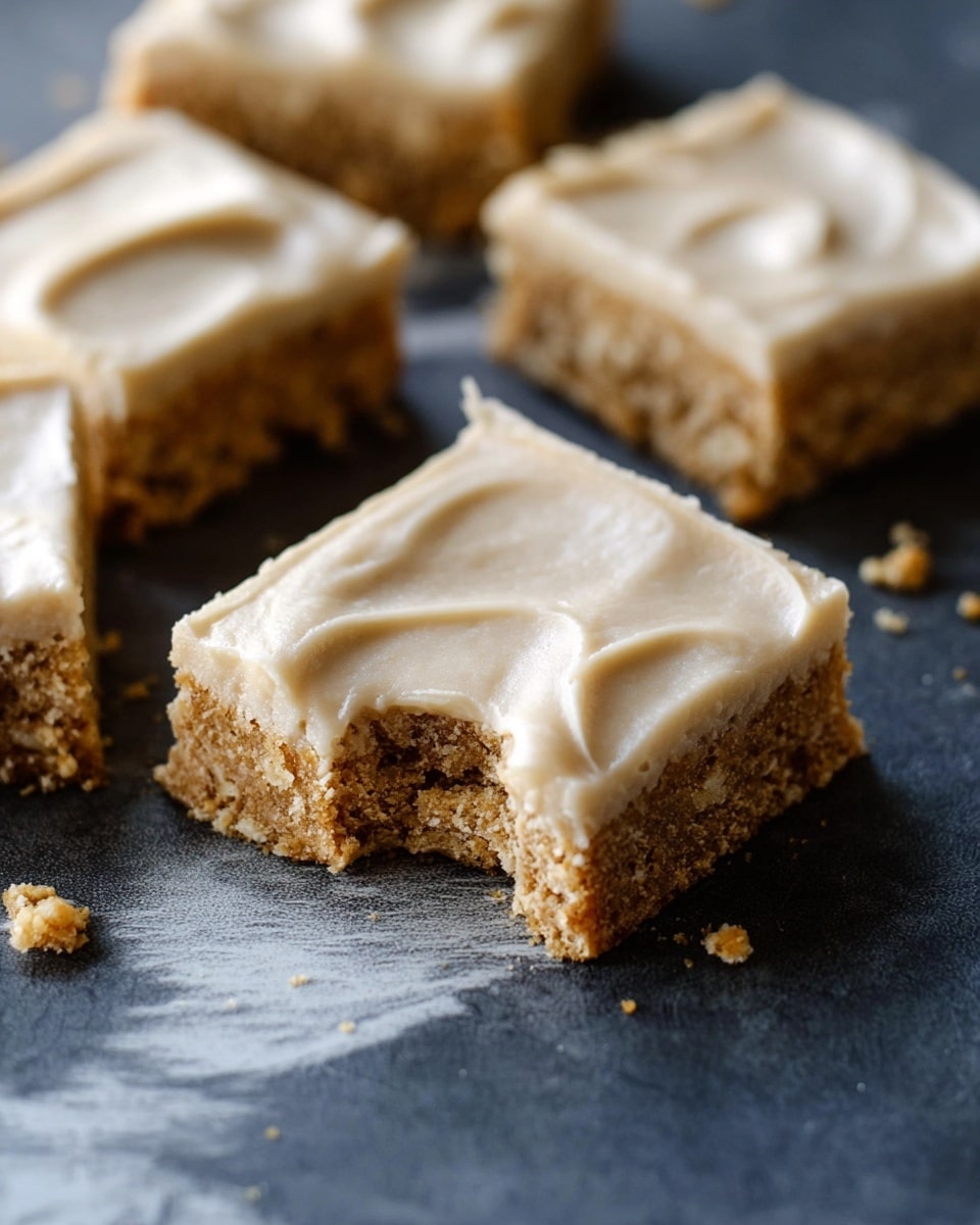 The image shows several square-shaped dessert bars with two distinct layers placed on a dark surface with white marbled texture. The bottom layer is crumbly and light brown with a rough texture that looks like a cookie or oat base. The top layer is thick and smooth with a creamy light tan color, spread evenly with soft swirls. The bars are arranged close to each other, and small crumbs are scattered around them. photo taken with an iphone --ar 4:5 --v 7