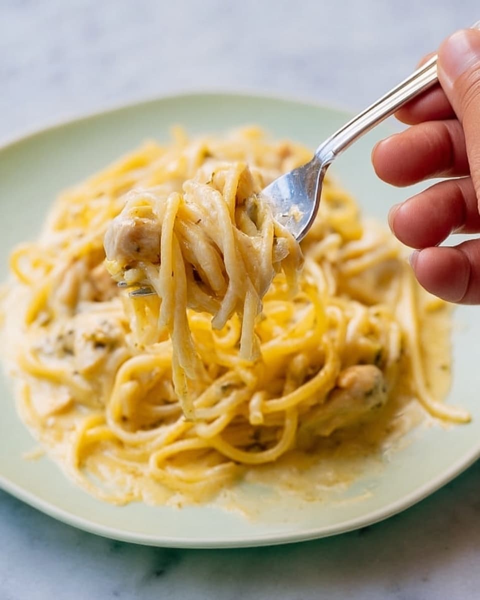 A red casserole dish with white floral and bird patterns holds a baked noodle casserole with three visible layers: the top layer is golden melted cheese mixed with light brown shredded chicken pieces and small green vegetable bits; below is a creamy, pale yellow noodle layer with intertwined spaghetti strands and some red and green bits; the bottom layer appears to be a rich, slightly saucy mix. The dish is placed on a folded red cloth with a subtle pattern, sitting on a white marbled texture surface. In the background, colorful floral patterned white bowls and clear glassware are softly blurred. photo taken with an iphone --ar 4:5 --v 7