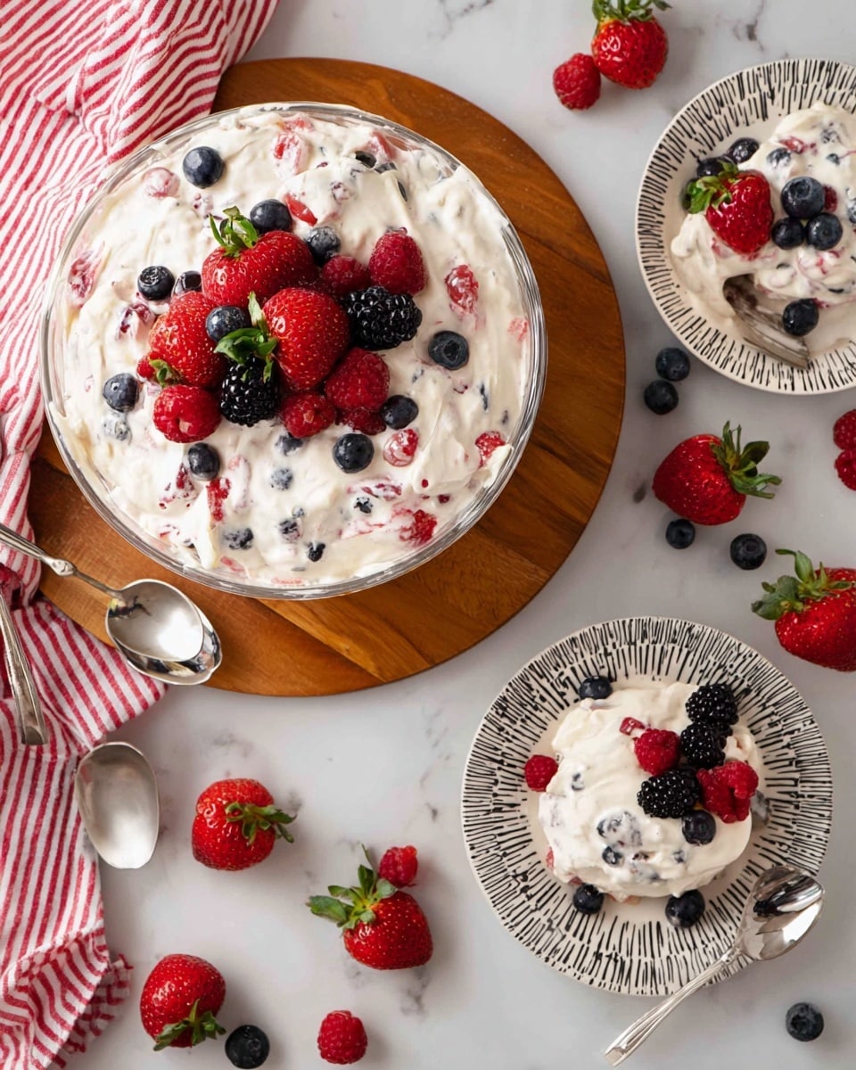 A large glass bowl filled with a creamy white whipped mixture with small pieces of mixed berries inside. On top of the mixture is a colorful pile of fresh berries, including bright red strawberries with green leaves, dark blackberries, deep blue blueberries, and bright red raspberries, all scattered together. In the background, there is a white container filled with more strawberries, and a small glass jar holding red raspberries placed on a white marbled surface with a red and white checkered cloth nearby. Photo taken with an iphone --ar 4:5 --v 7