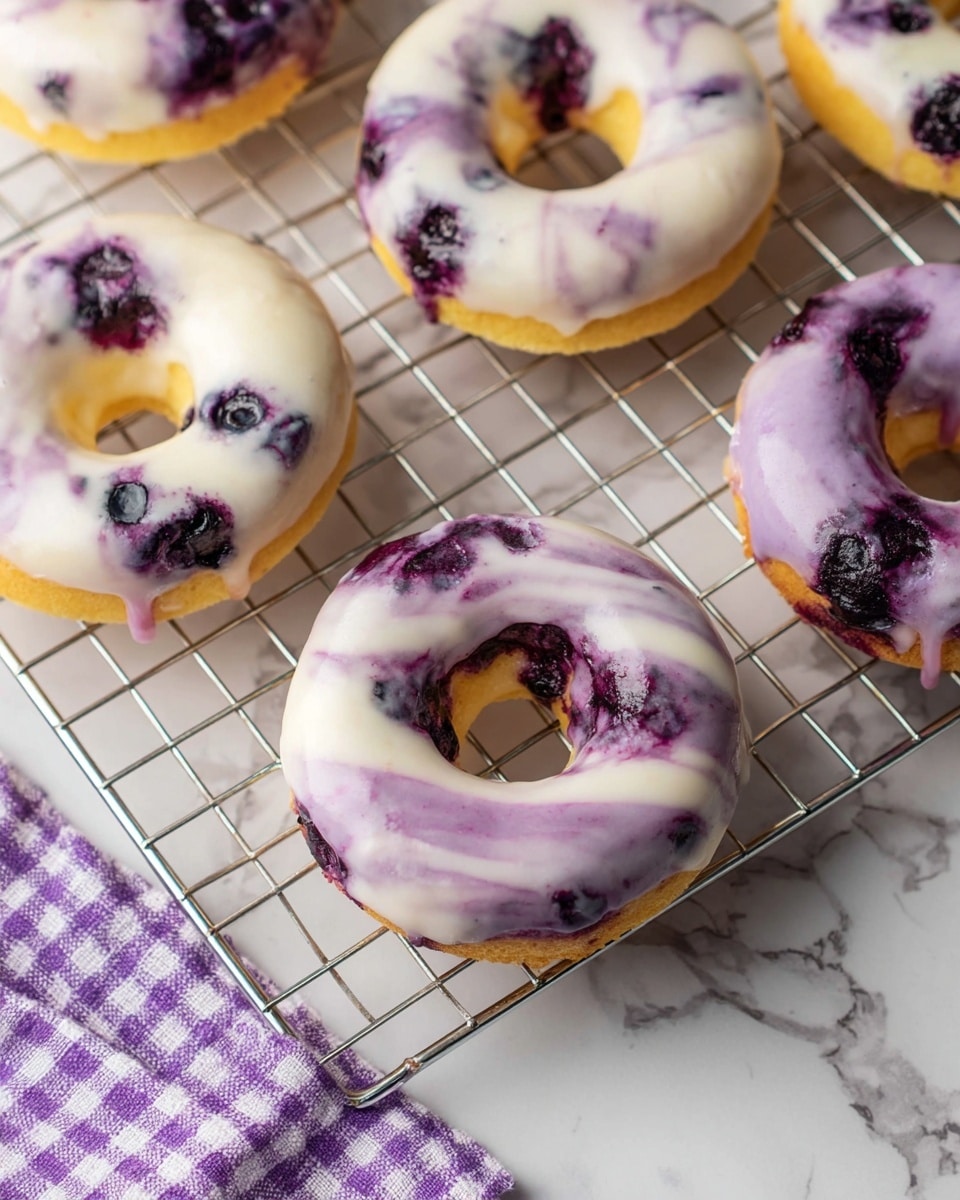 Six blueberry donuts rest on a silver cooling rack over a white marbled surface. Each donut has a yellow cake base with a glossy glaze on top, swirling with colors of creamy white and soft purple mixed with visible blueberry bits. The donuts are arranged in two vertical columns and three horizontal rows, showing a mix of darker and lighter glaze patterns that highlight the blueberry texture. Around the rack, there are scattered fresh blueberries, purple and pink flowers, and a partial view of a white plate and a purple checkered cloth. Photo taken with an iphone --ar 4:5 --v 7