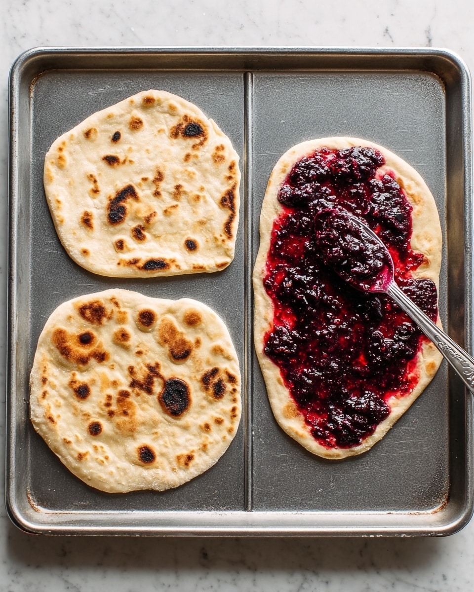 Two slices of blueberry flatbread are placed on a white plate resting on a white marbled surface. Each slice has three visible layers: a golden-brown crust as the base, a top layer of deep purple blueberry topping with whole blueberries scattered across, and dollops of white cheese spread unevenly over the berries, creating a textured contrast. Fresh green mint leaves are placed on top of each slice, with a few loose blueberries and mint leaves scattered around the plate. A small white bowl filled with glossy dark blueberry sauce is partially visible nearby. photo taken with an iphone --ar 4:5 --v 7
