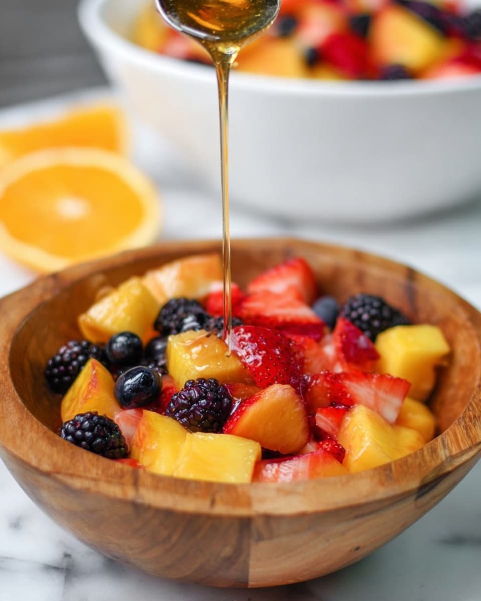 A wooden bowl filled with three layers of colorful fruit pieces: the bottom layer has orange peach chunks with smooth skin and soft texture, the middle layer contains bright red sliced strawberries with visible seeds and juicy flesh, and the top layer has dark purple blackberries and round blueberries with a shiny surface. A golden syrup is being poured from above onto the fruit, creating a thin stream that adds a glossy shine. The bowl sits on a white marbled surface, with parts of sliced oranges visible around it. In the background, a large white bowl with more mixed fruit is slightly blurred. Photo taken with an iphone --ar 4:5 --v 7