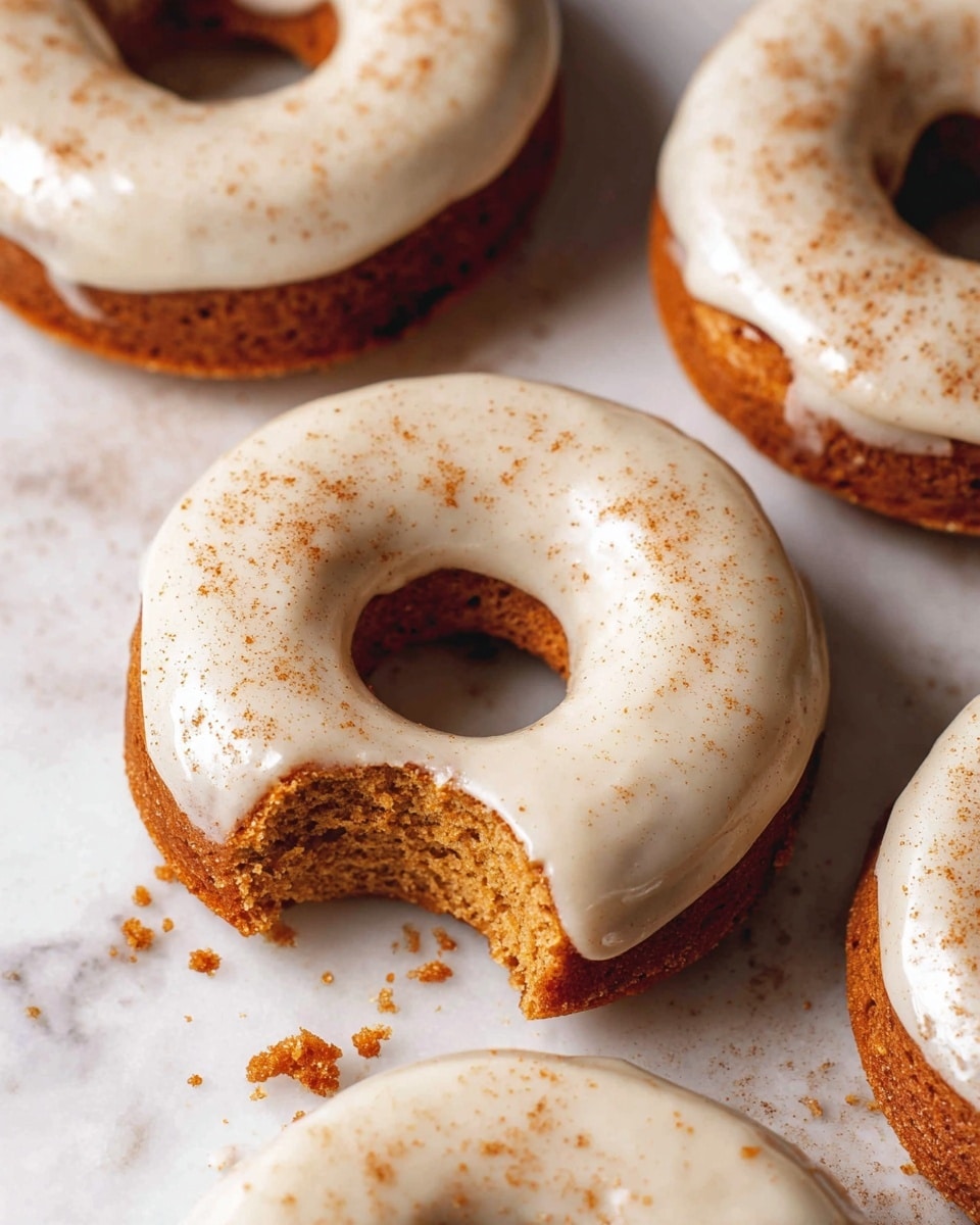 Four donuts are shown on a white marbled surface, each donut has a light brown cake base and is topped with a thick, creamy white glaze that covers the top half. The donut in the front has a bite taken out, revealing a soft, moist crumb inside, and a few crumbs scattered around it. The glaze on all donuts is smooth and slightly shiny, while a light dusting of a brown powder is sprinkled on top. The photo is close-up, focusing on the textures and details of the donuts. photo taken with an iphone --ar 4:5 --v 7