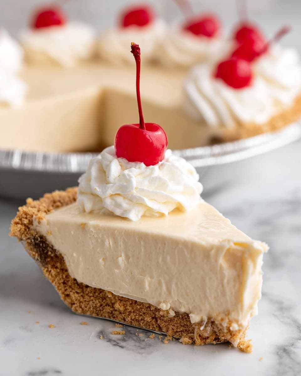 A slice of creamy beige pie with a crumbly light brown crust at the bottom forms the base layer. On top, there is a thick smooth pale cream filling layer that looks soft and airy. The pie slice is topped with a small dollop of white whipped cream that has a fluffy texture. Sitting on the whipped cream is a bright red cherry with a long thin stem standing upright. In the background, the rest of the pie is visible, also decorated with whipped cream and red cherries. The pie is in a foil pan on a white marbled surface. Photo taken with an iphone --ar 4:5 --v 7