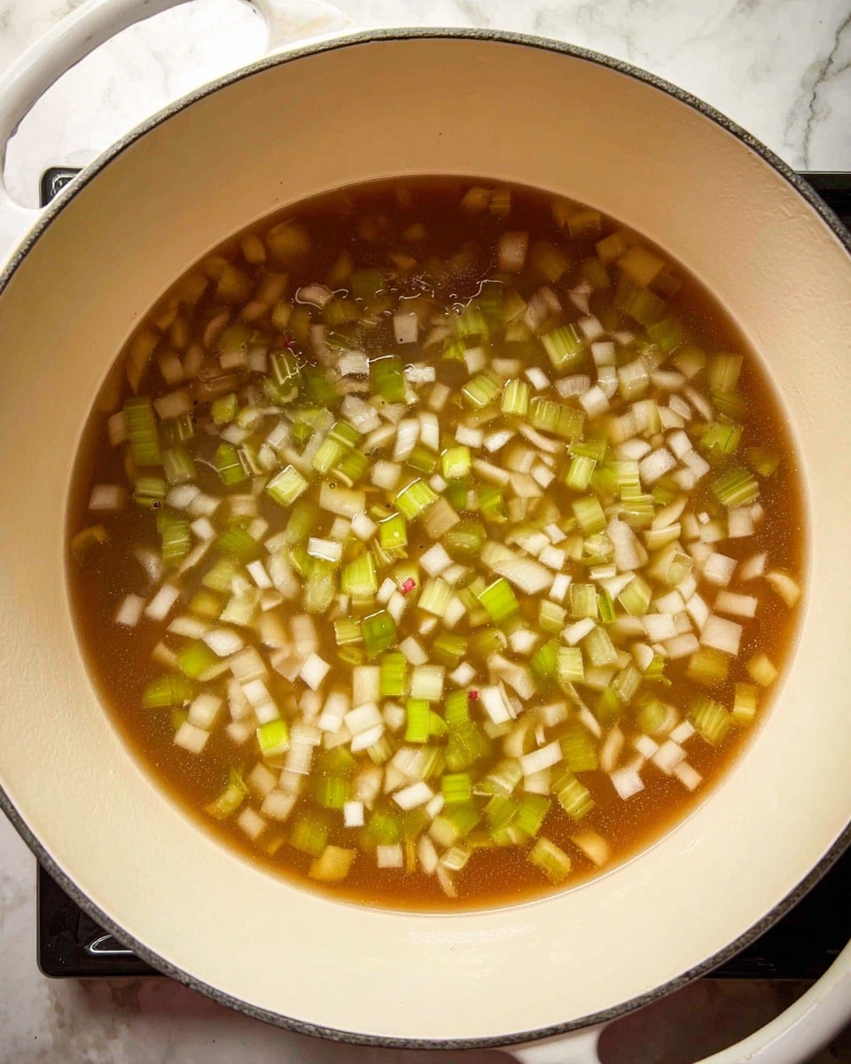The image shows a large white pot filled with a clear brown broth. Inside the broth, there are two visible layers of diced vegetables: the first layer has small, pale white and light grey pieces, and the second layer has light green slices of celery scattered evenly throughout. The pot is positioned on a stove with a white marbled surface barely visible at the bottom edges. photo taken with an iphone --ar 4:5 --v 7