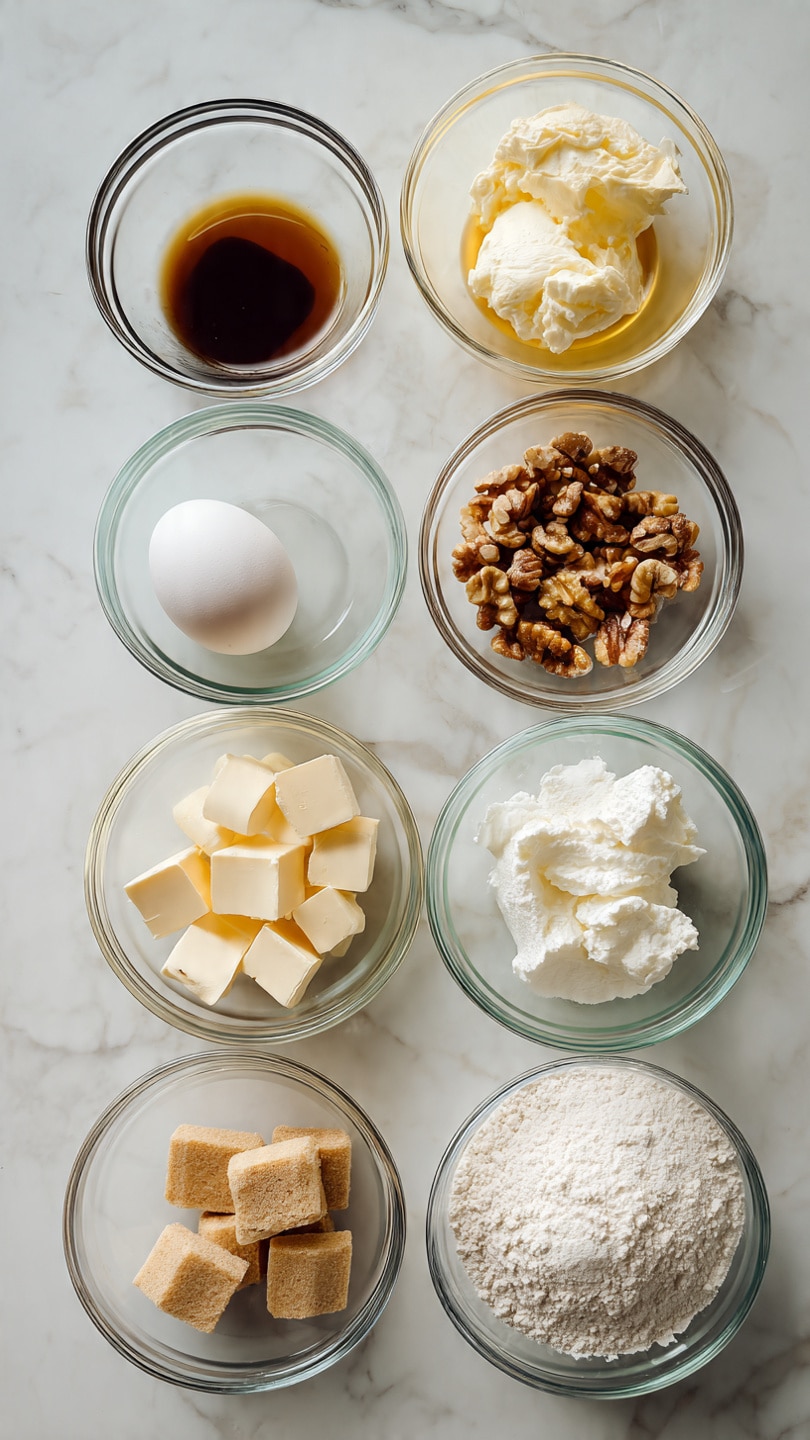 The image shows nine clear glass bowls and one egg on a white marbled surface. From the top left corner moving right, there is a small bowl with dark brown vanilla extract, a medium bowl with melted yellow butter, a medium bowl with white cream cheese, a white egg, and a medium bowl filled with chopped brown nuts. Below these, from left to right, there is a small bowl with white cream, a medium bowl filled with light brown sugar, a medium bowl with cubed pale yellow butter, and a medium bowl with white flour. The ingredients are neatly arranged in three rows. photo taken with an iphone --ar 4:5 --v 7