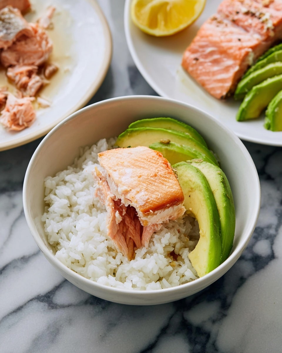 A round white bowl filled with a base layer of white rice topped with slices of green avocado and a piece of cooked pink salmon with a shiny, slightly brown glaze, positioned near the center of the bowl; in the background, there are two white plates placed on a white marbled surface, one containing a partially shown portion of cooked salmon with a pink center and brown crust, and the other holding slices of avocado and a lemon wedge. Photo taken with an iphone --ar 4:5 --v 7