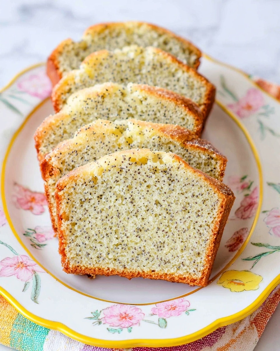 Five slices of lemon poppy seed cake are arranged on a white plate with pastel floral patterns and a yellow trim. Each slice shows a light golden brown crust with a moist, pale yellow interior speckled evenly with tiny black poppy seeds. The slices are placed upright, slightly leaning against each other in two rows, showcasing the even texture and soft crumb of the cake. The plate sits on a white marbled surface with a colorful cloth partially visible under it. photo taken with an iphone --ar 4:5 --v 7