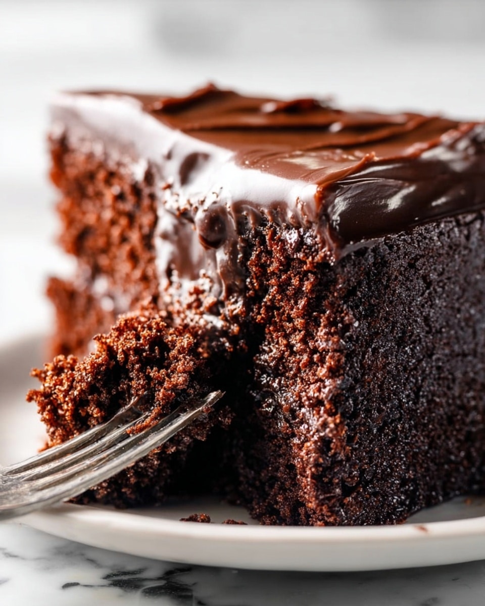 A close-up view of a thick slice of chocolate cake placed on a white plate, showing two main layers: a dense, dark brown chocolate cake base with a coarse texture and a smooth, shiny, dark chocolate frosting layer on top with a smooth finish. A silver fork held by a woman's hand is pressing into the cake from the right side, breaking the top frosting and the cake slightly, with some crumbs scattered on the plate. The background features a white marbled texture with soft lighting highlighting the rich chocolate tones. Photo taken with an iphone --ar 4:5 --v 7