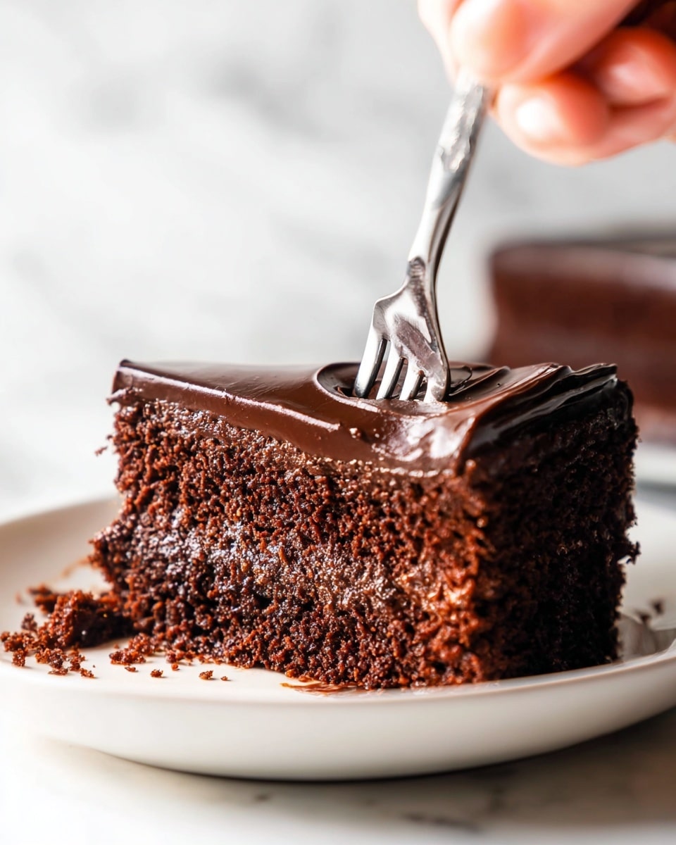 The image shows a close-up of a thick slice of chocolate cake with two layers. The bottom layer is a moist, dark brown chocolate sponge with a crumbly texture. The top layer is a smooth, glossy dark chocolate frosting with a rich, shiny finish. A silver fork is digging into the front of the cake slice, breaking the dense cake and frosting. The cake sits on a white plate placed on a white marbled surface. photo taken with an iphone --ar 4:5 --v 7