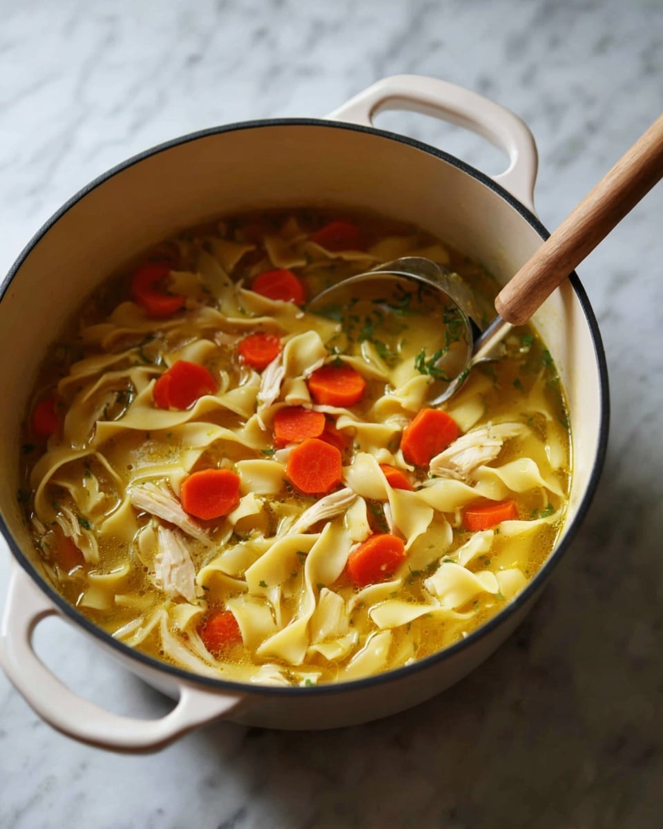 A white pot filled with three main layers: the bottom layer is a light yellow broth, the middle layer has wide, flat pale yellow noodles floating evenly throughout, and the top layer has small slices of bright orange carrots and small light beige chunks of chicken scattered on top and mixed inside. A wooden spoon with a light brown handle and a silver scoop rests on the right side inside the pot. The pot sits on a white marbled surface. Photo taken with an iphone --ar 4:5 --v 7