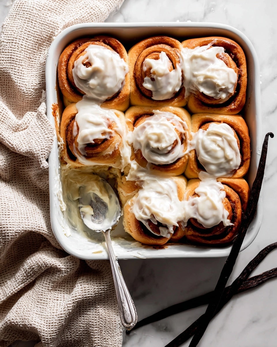 A close-up of a cinnamon roll with white icing on top, showing three visible layers inside in light brown and beige colors, with the outer layer soft and a bite taken out of it. Behind it, several more cinnamon rolls with white icing are placed on a piece of brown parchment paper on a white marbled surface. To the side, there is a white bowl with a spoon in it, and two dark brown vanilla pods lie next to the cinnamon roll in the foreground. Photo taken with an iphone --ar 4:5 --v 7