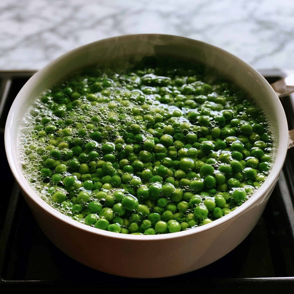 A white bowl filled with small twisted pasta all coated in a thick bright green sauce that looks smooth and creamy. The pasta is sprinkled lightly with black pepper and there is a small wedge of lemon placed on the rim of the bowl. Fresh green leaves are visible near the pasta, adding a fresh touch. The bowl sits on a white marbled surface beside a half lemon and a soft cloth with a checked and scalloped edge pattern. The scene is simple and fresh looking with natural light. photo taken with an iphone --ar 4:5 --v 7