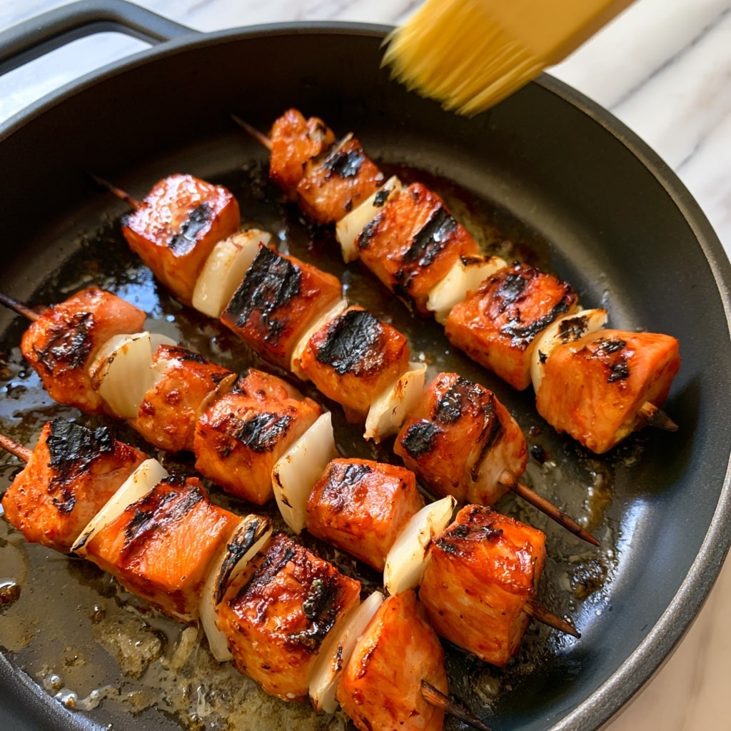 The image shows four wooden skewers of grilled chicken tikka placed on a round white plate. Each skewer has three main sections of orange-red grilled chicken pieces with clear char marks, separated by chunks of white paneer cheese and purple onion pieces, all assembled in a repeating pattern. Each skewer is garnished with small green coriander leaves. Around the plate, there are small bowls containing two types of sauces, one dark green and chunky, the other light green and smooth with some brown spots on the surface. To the right, there is a black bowl filled with sliced purple onions and green leaves, along with lemon halves scattered around. The setting sits on a white marbled surface. Photo taken with an iphone --ar 4:5 --v 7