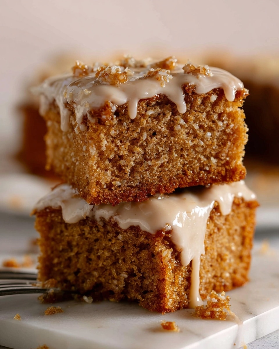 Several square pieces of moist brown cake with a rough texture and bits of nuts inside are placed on a white plate. Each piece has a thick layer of light tan creamy frosting on top, some parts showing bits of nuts mixed into the frosting. The background is a white marbled texture. photo taken with an iphone --ar 4:5 --v 7