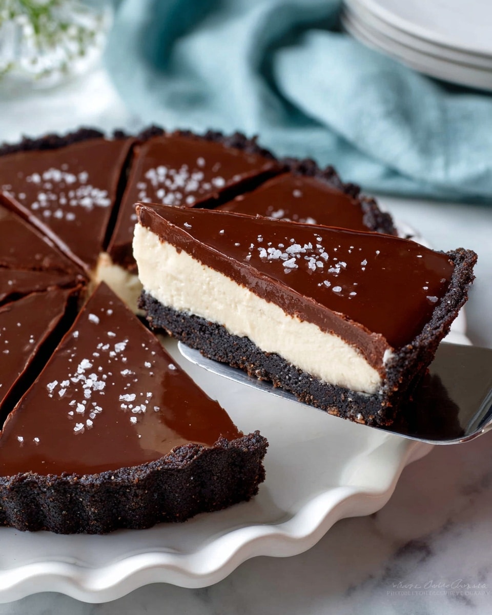 A slice of dark chocolate tart with three visible layers sits on a white plate with scalloped edges. The bottom layer is a thin, crumbly dark cookie crust, the middle layer is a thick creamy white filling, and the top layer is a smooth, shiny dark chocolate ganache sprinkled with coarse sea salt flakes. The tart is cut into even slices with one slice being lifted on a metal spatula, showing clean edges and the layers in clear view. The background is a white marbled texture, and a soft light blue cloth is seen blurred in the top part of the image. photo taken with an iphone --ar 4:5 --v 7