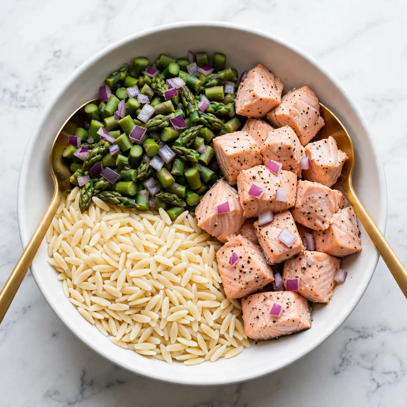A white bowl holds a dish with three main layers carefully placed next to each other. On the left bottom side, there is a layer of small pasta shaped like rice grains, pale cream in color with a smooth texture. Above the pasta, chopped green asparagus pieces form a thick layer with some purple onion bits scattered over them, giving a mix of green and purple shades with a soft, cooked texture. To the right, there is a pile of cooked salmon chunks in soft pink tones, lightly seasoned with black pepper and bits of purple onion. The layers do not overlap much, and two gold-colored serving spoons rest in the bowl, one on the left and the other on the right. The dish sits on a white marbled surface. Photo taken with an iphone --ar 4:5 --v 7