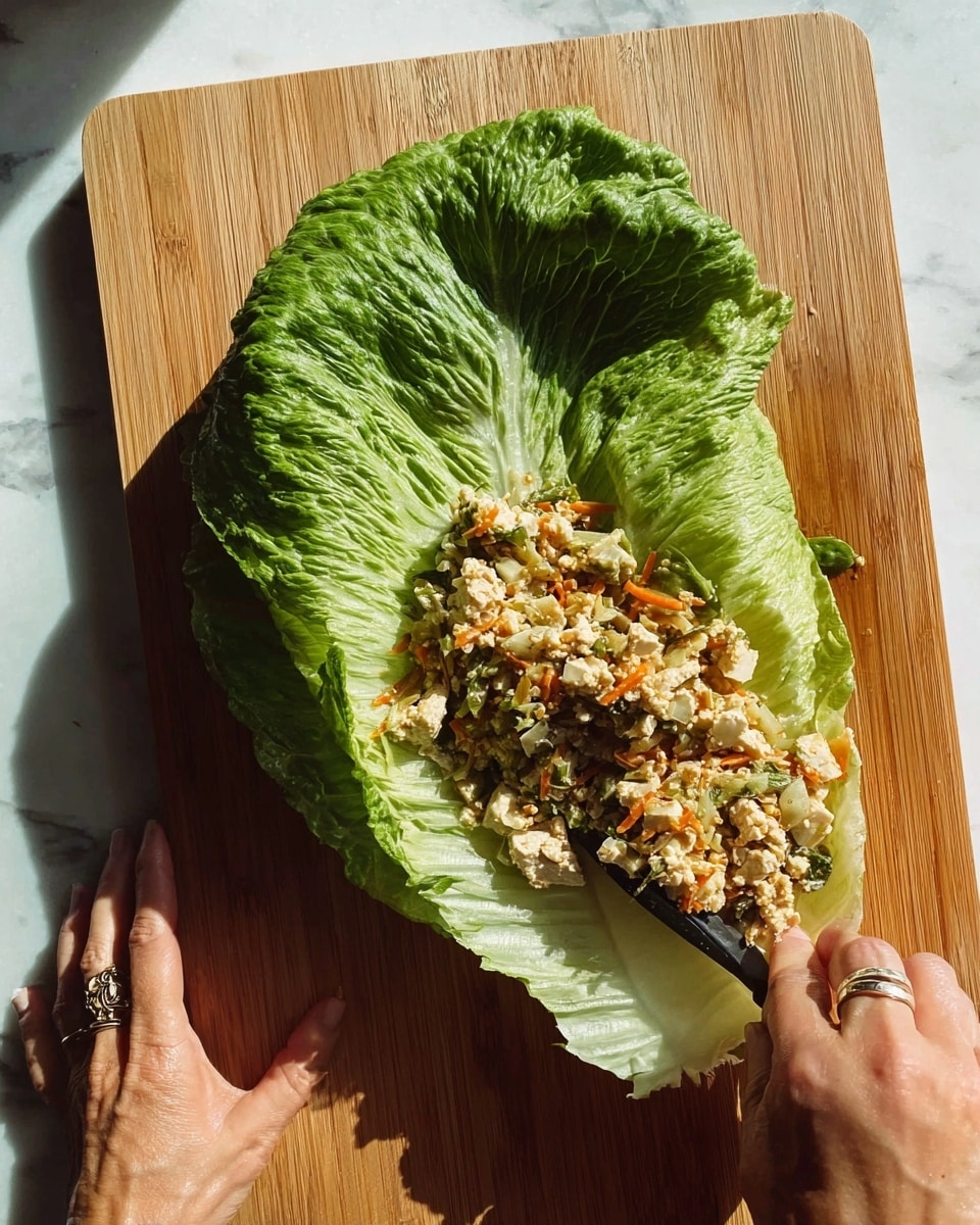 The image shows several rolled cabbage leaves with a light green and white color, filled and cooked until slightly browned on the edges. They are placed in a shallow pool of bright reddish-orange sauce with visible chili flakes and oil. One roll is held close to the camera by shiny silver chopsticks, showing the texture and slight charring on the cabbage leaves. The cabbage rolls sit on a white plate on a white marbled surface, with two soft pink vases blurred in the background. Photo taken with an iphone --ar 4:5 --v 7