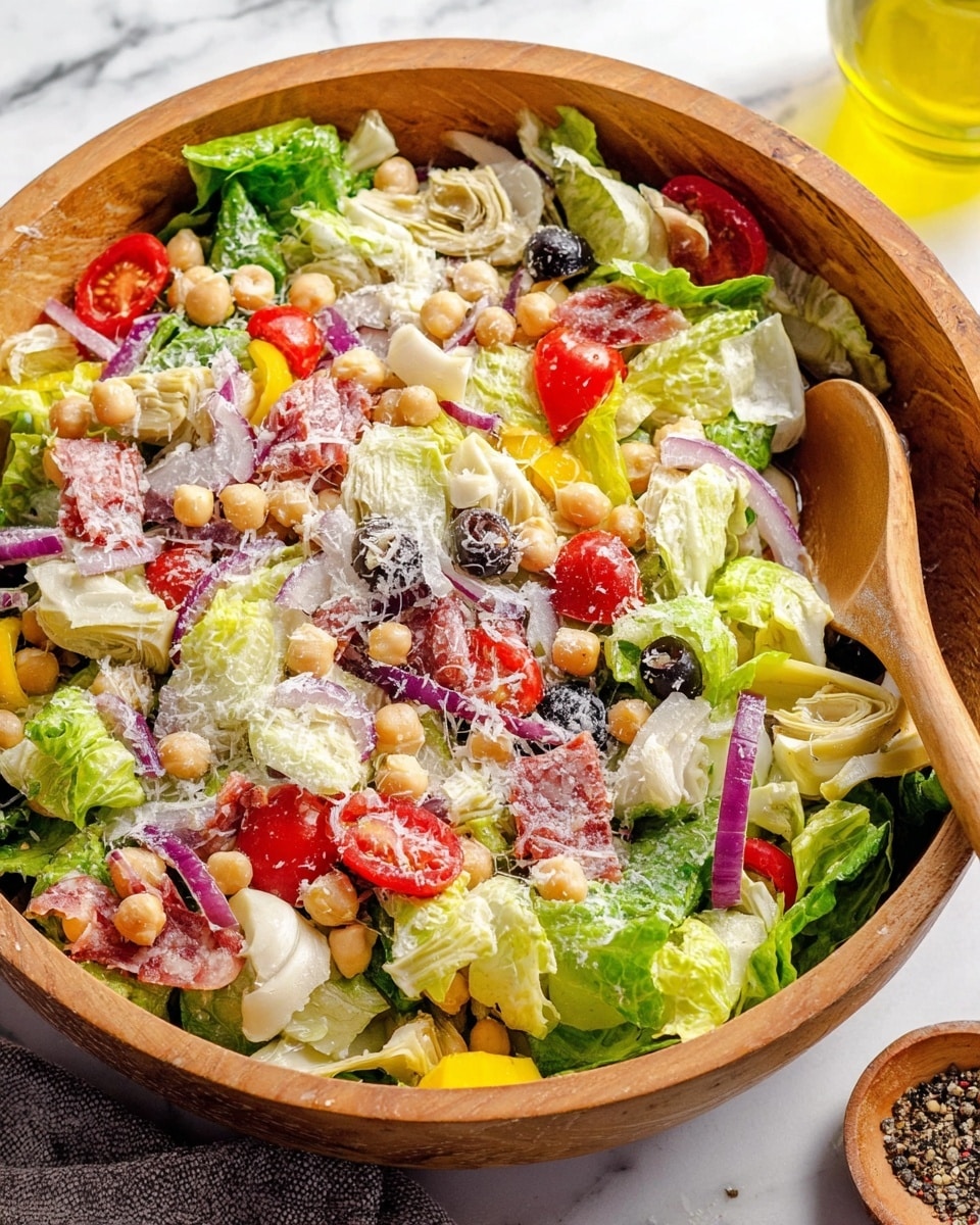 A large wooden bowl filled with a colorful mixed salad showing many layers and textures: the base is bright green romaine lettuce leaves, topped with slices of pale green and white artichoke hearts, dark purple olive pieces, red cherry tomato halves, thin rings of purple onion, and pale yellow pepper slices. Small round chickpeas and chunks of light green cucumber are scattered throughout. The salad is sprinkled with grated white cheese and drizzled with a light golden dressing. Two wooden salad spoons rest inside the bowl, placed on a white marbled surface with small white and black pepper dishes nearby. Photo taken with an iphone --ar 4:5 --v 7