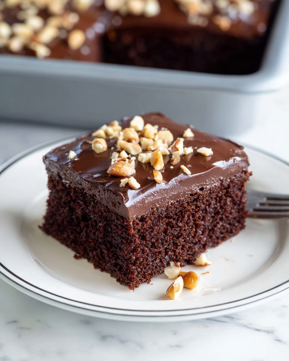 A thick square piece of rich dark brown chocolate cake with a smooth layer of shiny chocolate frosting on top, sprinkled with chopped light tan nuts, is held up by a spatula over the remaining cake which shows the same frosting and nut topping covering the surface. The cake texture looks soft and moist with tiny air holes visible in the crumb. In the blurred background, a white plate holds another piece of the cake, and there is a glass with milk on the white marbled surface. Photo taken with an iphone --ar 4:5 --v 7