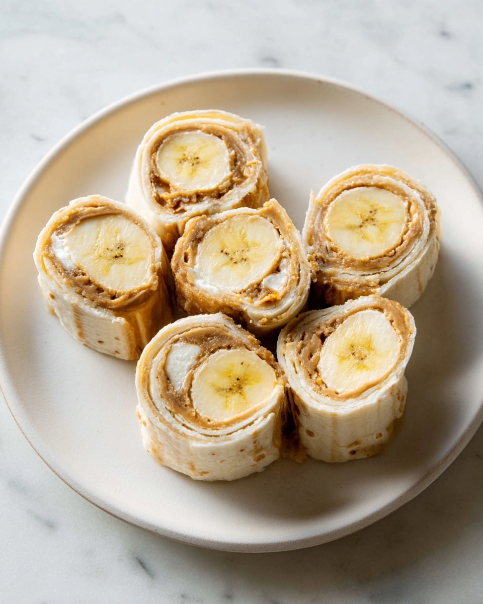 Six round slices are arranged on a white plate with a soft texture. Each slice has three visible layers: the innermost is a pale yellow banana slice with a smooth texture, the middle layer is a light brown creamy spread, and the outer layer is a slightly toasted beige wrap with a thin, soft texture. The plate sits on a white marbled surface. photo taken with an iphone --ar 4:5 --v 7