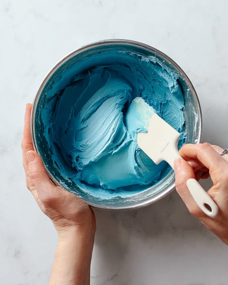 A clear glass dish contains scoops of a colorful dessert with light blue and white creamy layers mixed with cake pieces dotted with bright multicolored sprinkles, creating a marbled effect. The texture looks soft and melted around the edges with some areas showing chunkier cake parts, and the dessert fills about half the dish. Around the dish on a white marbled surface are cupcakes topped with vivid blue frosting and small sprinkles, adding a festive touch. photo taken with an iphone --ar 4:5 --v 7