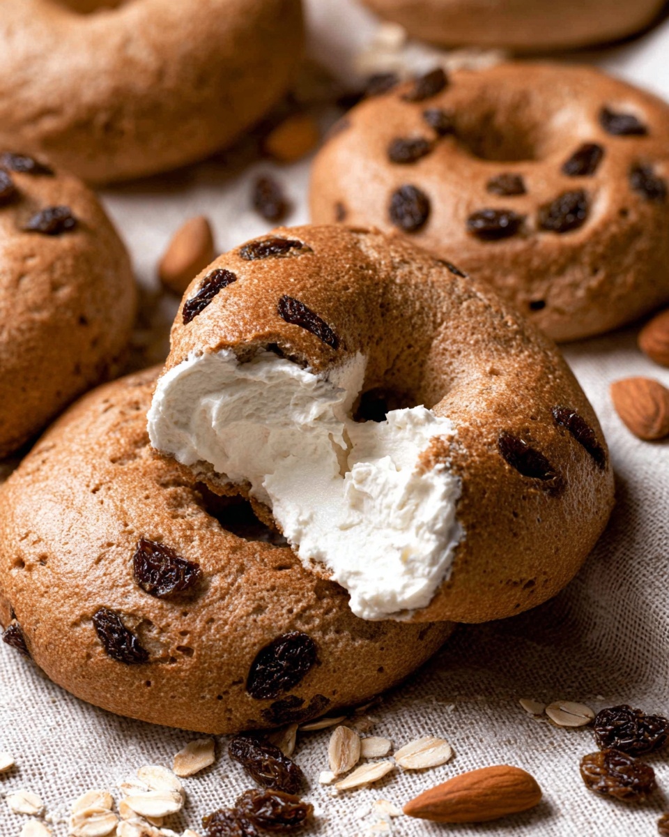 The image shows five round raisin bagels with a golden brown, slightly rough texture, each having a hole in the center and raisins visible on the surface. Two bagels are whole, and three are opened, with one split piece spread with a thick layer of white cream cheese. Scattered around the bagels are almonds, cinnamon sticks, and loose raisins on a beige woven cloth that covers a white marbled surface. In the background, there are two clear glass bowls, one filled with white cream cheese and the other with raisins. photo taken with an iphone --ar 4:5 --v 7