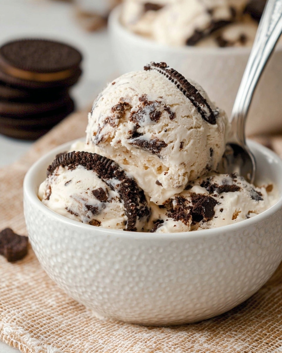 A white textured small bowl filled with a large scoop of creamy vanilla ice cream mixed with dark chocolate cookie bits, creating a marbled pattern of white and dark brown. Leaning against the ice cream inside the bowl is a halved chocolate sandwich cookie with a white cream center. Around the bowl on a white marbled textured surface, several whole and broken chocolate sandwich cookies with white cream centers lie scattered, along with a few small dark chocolate chips. A metal spoon is placed inside the bowl, angled outward. In the background, there is a white plate stacked with more chocolate sandwich cookies. photo taken with an iphone --ar 4:5 --v 7