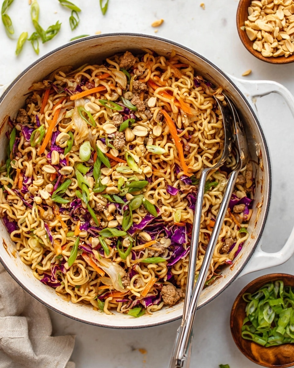A large white pot filled with a colorful noodle stir-fry. The bottom layer shows light brown curly noodles mixed with thin strips of bright orange carrot and slices of purple and white cabbage scattered throughout. Small light brown chunks of cooked meat are mixed evenly in the noodles. On top, there are bright green sliced scallions and chopped light tan peanuts sprinkled for garnish. Two shiny silver utensils rest inside the pot, slightly buried in the noodles. Around the pot on a white marbled surface are scattered slices of scallion and a small wooden bowl filled with chopped peanuts. photo taken with an iphone --ar 4:5 --v 7