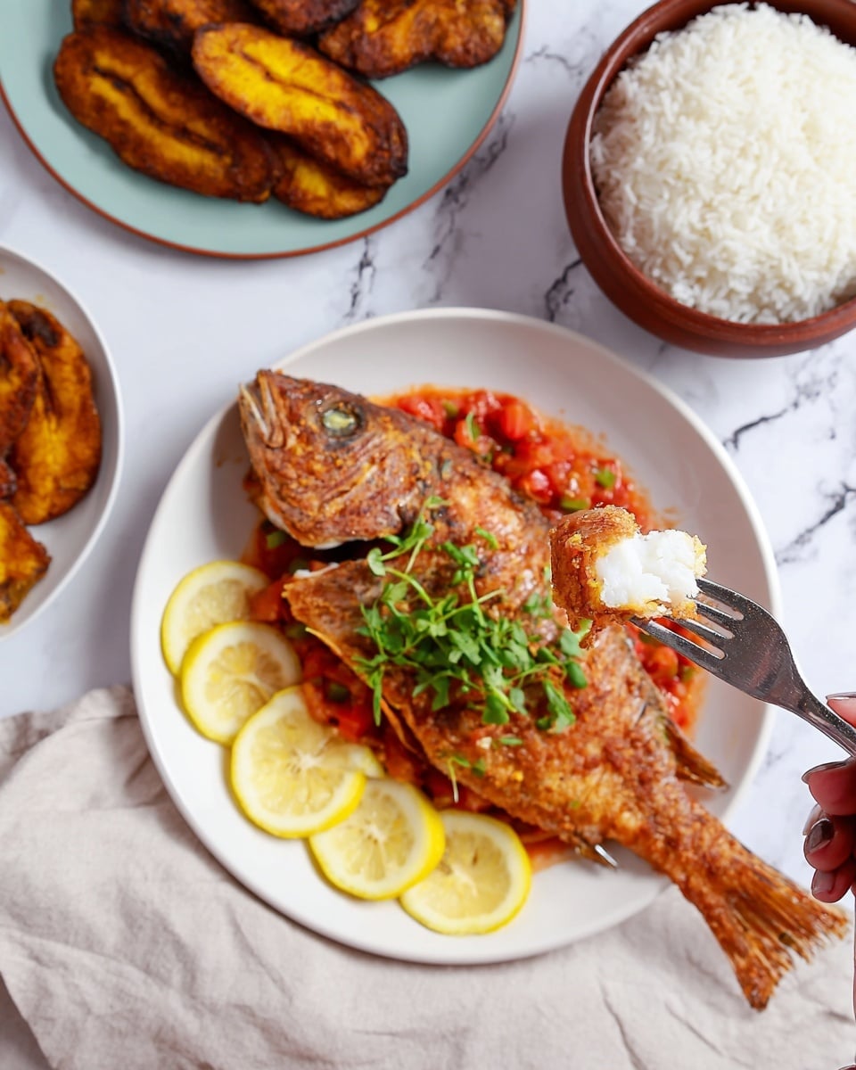 A white plate holds one whole fried fish with a crispy golden-brown textured skin, placed on a layer of chunky red tomato sauce. On the front side of the fish are six lemon slices arranged in a curved line. A small bunch of fresh green cilantro sits on top of the fish near its head. To the left, another white plate contains a pile of golden-brown fried plantain slices, some darker with a slightly charred look, resting on a white paper towel. On the top right, a large brown bowl is filled with fluffy white rice and has a wooden spatula resting inside. All items are on a white marbled surface with a light cloth underneath the plates. Photo taken with an iphone --ar 4:5 --v 7