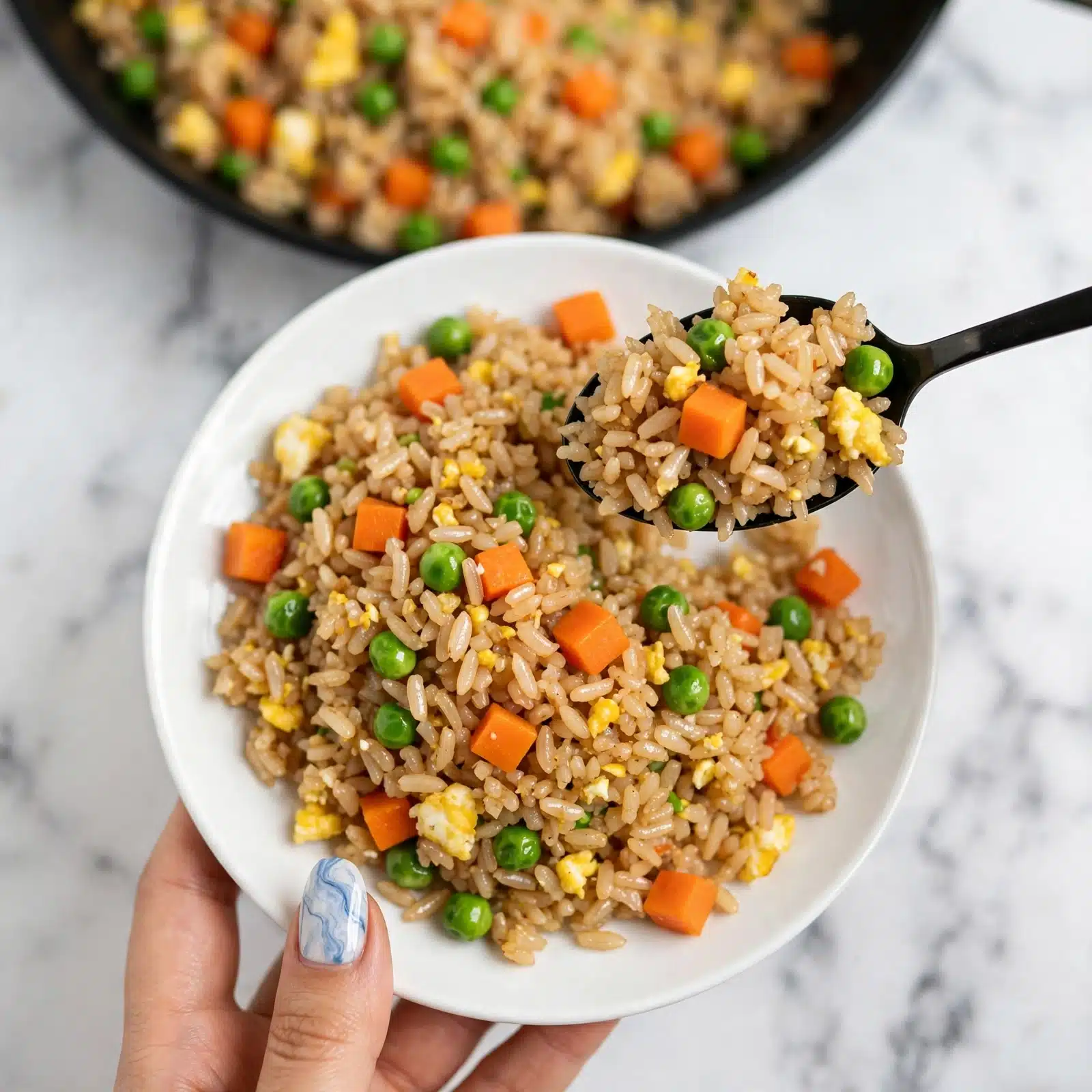 A close-up view of a black textured bowl filled with fried rice that has three main layers visible: the base layer is light brown rice, the middle layer has small orange carrot cubes scattered throughout, and the top layer includes bright green peas and small pieces of yellow scrambled egg mixed evenly with the rice. The bowl sits on a flat surface with a white marbled texture, and two whole fortune cookies are placed nearby on the surface, adding a light beige color contrast. Photo taken with an iphone --ar 4:5 --v 7